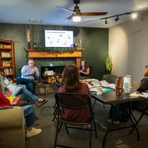 Attendees around folding tables watch the female trainer present the Currency and leadership philosophy slide at the Wichita PCM® workshop.
