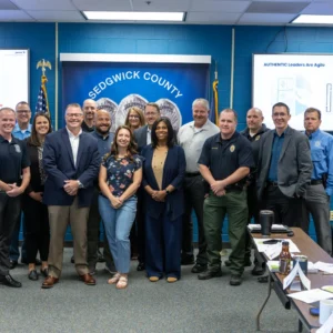Group portrait of Wichita PCM® workshop participants and Affinity Consultants trainers before a Sedgwick County banner and Authentic Leaders Are Agile slide.