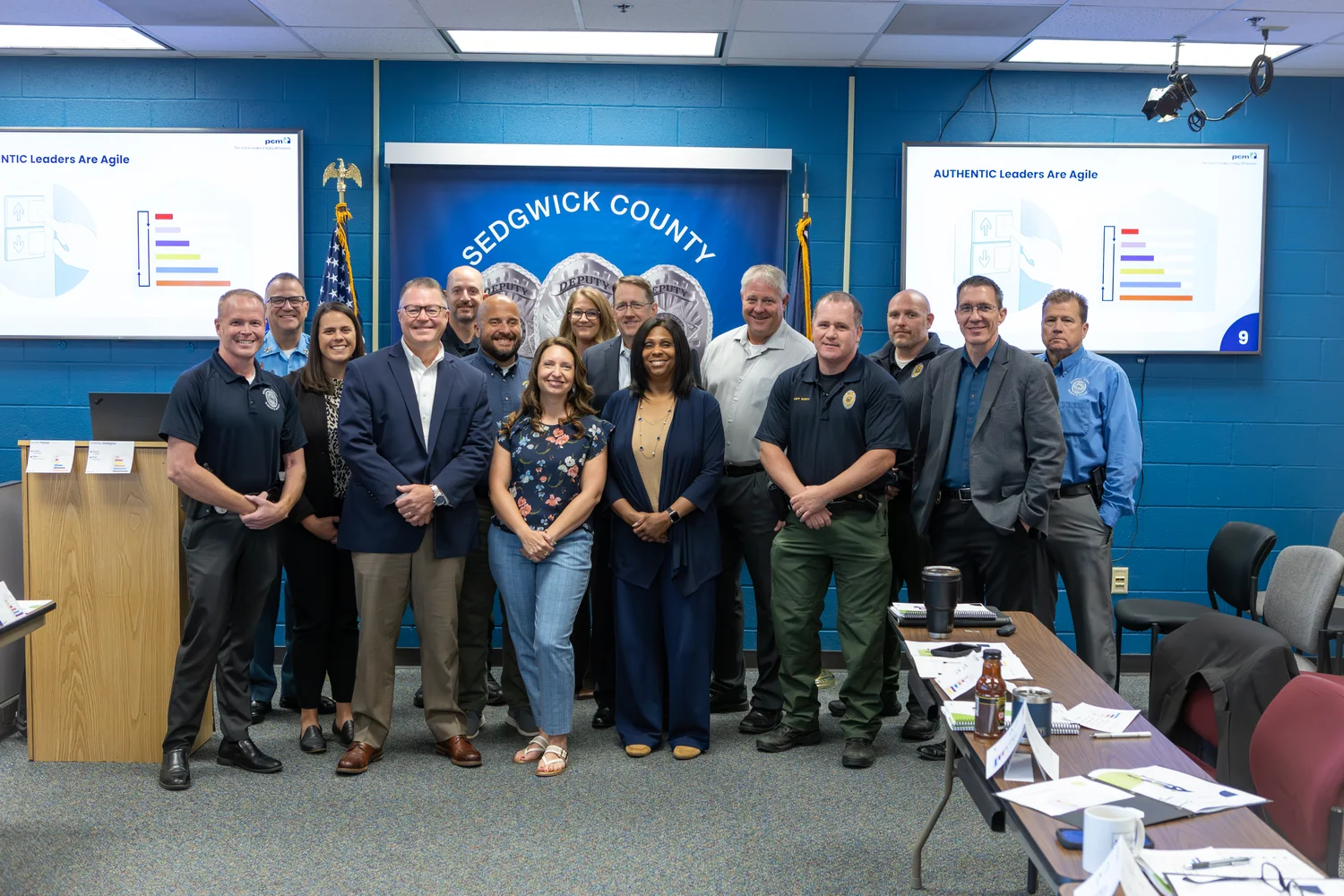 Group portrait of Wichita PCM® workshop participants and Affinity Consultants trainers before a Sedgwick County banner and Authentic Leaders Are Agile slide.