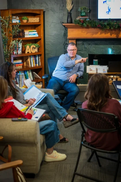 Male trainer speaks with hand on chest, engaging sofa-seated participants during the Wichita PCM® communication workshop.