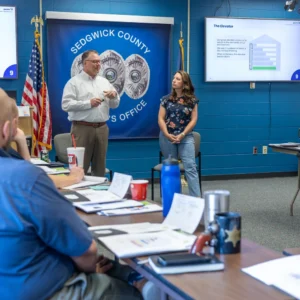 Two presenters lead a PCM® Elevator discussion in front of the Sedgwick County banner as officers listen at the Wichita training.