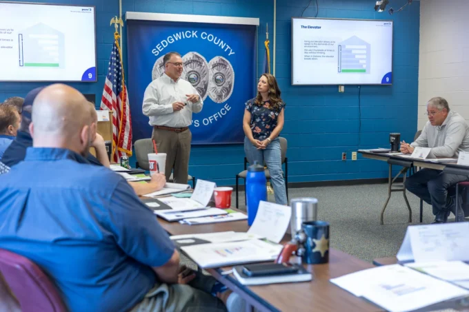 Two presenters lead a PCM® Elevator discussion in front of the Sedgwick County banner as officers listen at the Wichita training.
