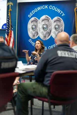 Sarah Thome gestures expressively while presenting to deputies beneath the Sedgwick County banner at the Wichita PCM® communication training.