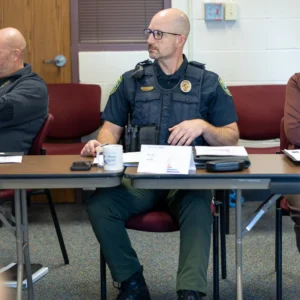 A silver-haired sheriffs captain in a light blue uniform listens attentively beside colleagues at the Wichita PCM® workshop.