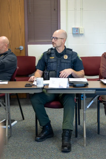 A silver-haired sheriffs captain in a light blue uniform listens attentively beside colleagues at the Wichita PCM® workshop.