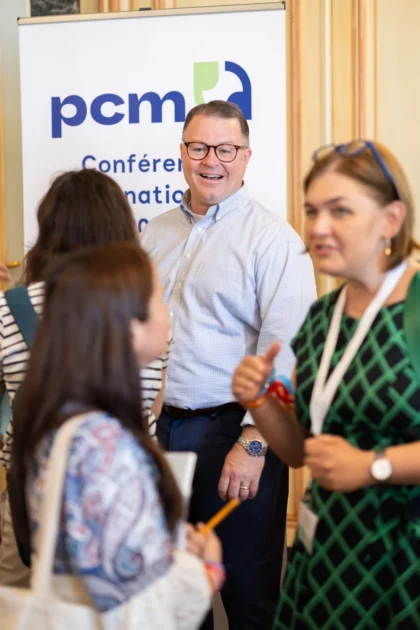 Affinity Consultants Matt Gallagher smiles in conversation with two women beside the banner at the Bordeaux PCM® conference.