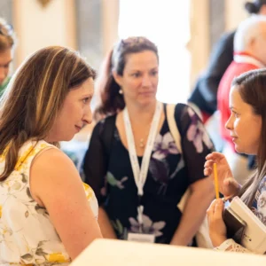 Sarah Thome and colleagues in animated small-group conversation among lanyard-wearing attendees at the PCM® International Conference in Bordeaux, France.
