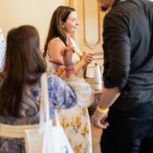 A woman in a yellow floral dress talks with a bearded man, a PCM® tote bag in the foreground, at the Bordeaux conference.