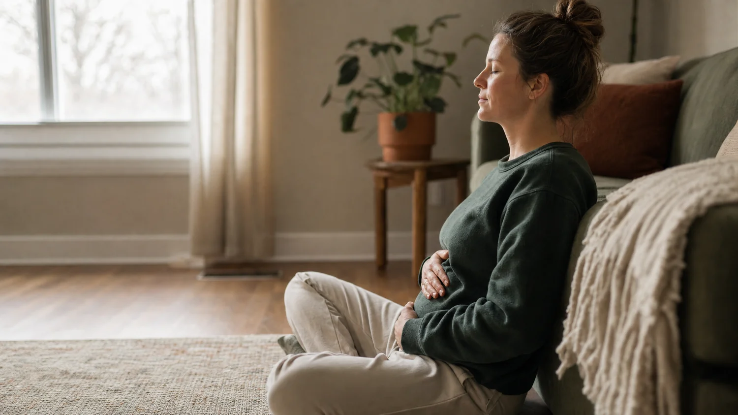 Side profile of a white / Caucasian person seated on the floor leaning against the side of a sofa mid-breathing-exercise